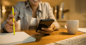 Pessoa usando celular e anotando informações, relacionada ao controle de finanças.